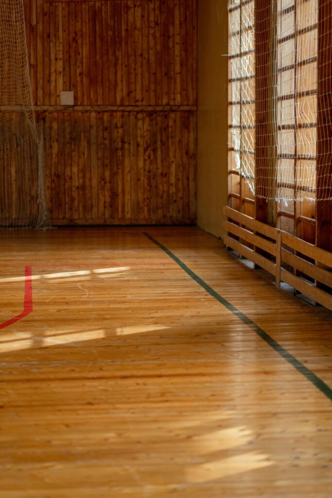 Empty gymnasium with polished wooden floor and sunlit walls, ideal for sports.